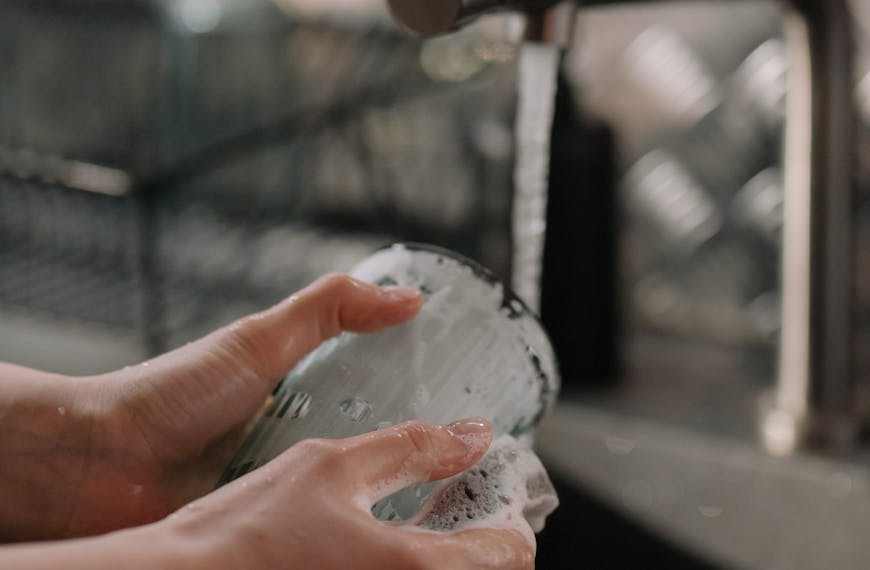 A close-up view of hands washing a glass under running water in a kitchen setting.