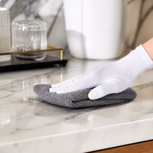 Femme de chambre experte utilisant une microfibre pour enlever la poussière sur un meuble en bois précieux.