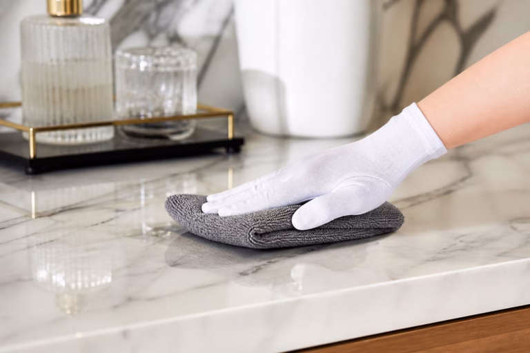 Femme de chambre experte utilisant une microfibre pour enlever la poussière sur un meuble en bois précieux.